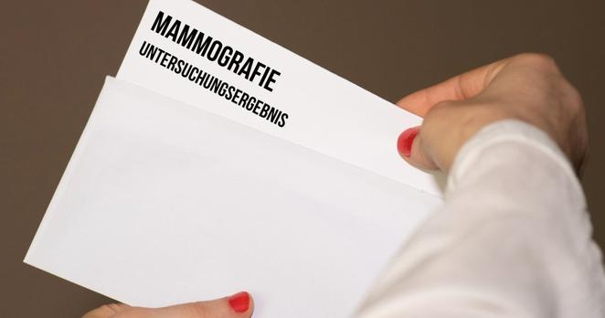 Eine Frau öffnet einen Umschlag mit den Ergebnissen einer Mammographie-Untersuchung.