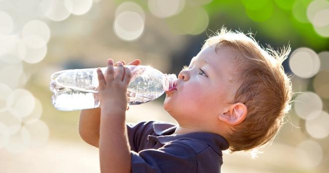 Ein kleiner Junge mit verschwitzten, blonden Haaren und einem blauen Polo-Shirt trinkt Wasser aus einer Plastikflasche
