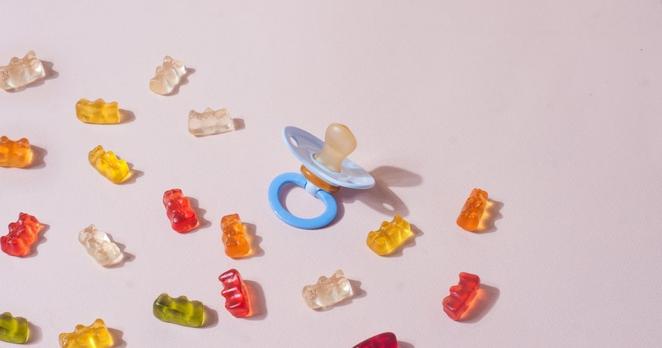Draufsicht: Gummibärchen und ein Schnuller liegen auf einem altrosafarbenen Hintergrund.