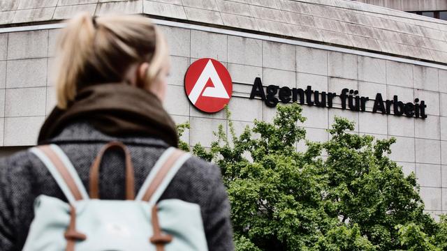 Eine junge Frau ist auf dem Weg zur Agentur für Arbeit und schaut auf das Logo des Gebäudes