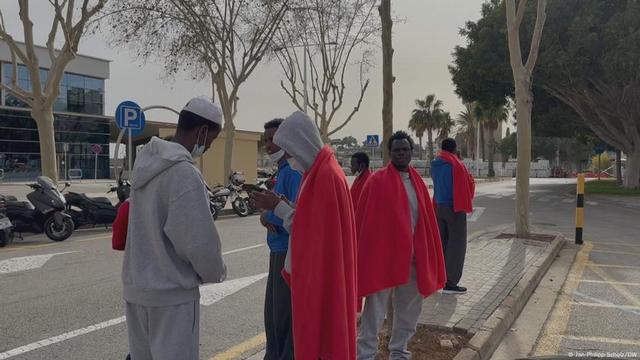 Flüchtlinge in rote Decken gehüllt stehen auf der Straße
