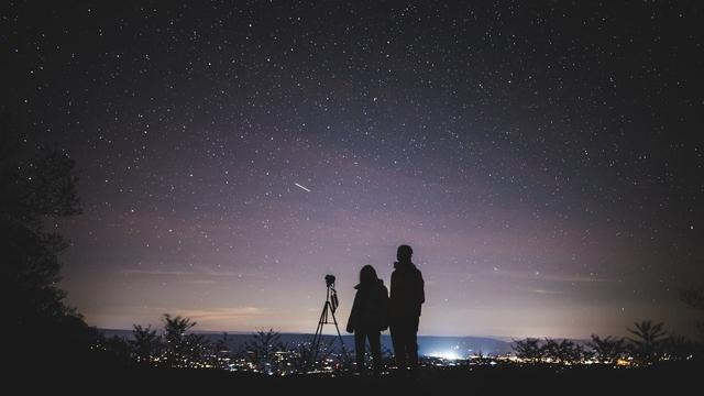 Pexels photo of 2 standing figures silhouetted on a hill at light, looking away from us, over the lights of a town in the distance below. They have a camera on a tripod. Above the town and filling most of the picture is a glorious blanket of stars in deep dark blues, grays & purples. At the center is a short streak in the sky, possibly the tail of a shooting star. Mood is one of serenity, anticipation, and cosmic wonderment. 
Captioned, "Silhouette of Two Persons Stargazing". 

Elkton, VA, United States, by Yuting Gao.  
www.Pexels.com/photo/silhouette-of-two-persons-stargazing-1567069/ 

www.KronoMoon.org 🏳️‍🌈 ☮️ 
#KronoWatch 