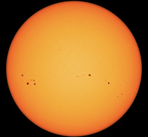 Die erdzugewandte Seite der Sonne in gelber bis orangeroter Farbe. In dieser Darstellung wirkt die Oberfläche glatt und strukturlos. Nur fünf oder sechs Sonnenflecken sind als dunkle Punkte darauf abgebildet, jeder von ihnen etwa von der Größe der Erde.
