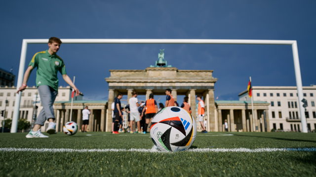 Ein Junge spielt vor dem Brandenburger Tor in Berlin Fußball.